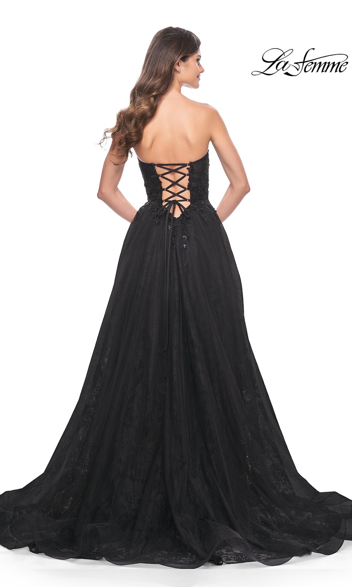 Woman wearing the La Femme Strapless Long Prom Ball Gown 31954 with a lace-up corset back, standing and facing away; La Femme logo is in the top right corner.